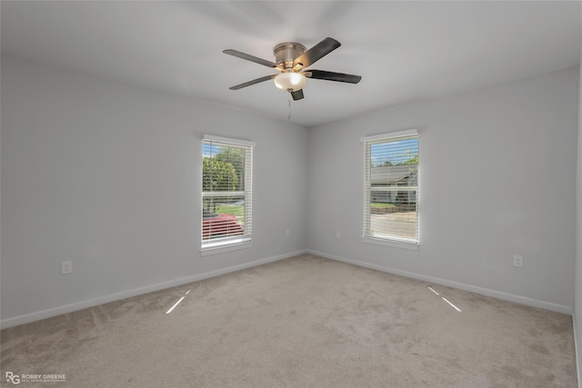 spare room with baseboards, a ceiling fan, and light carpet