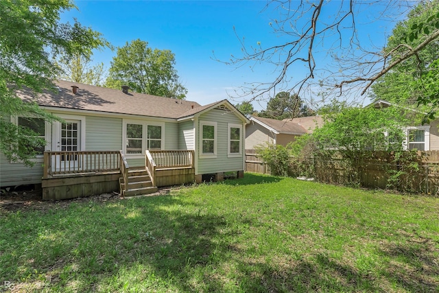 back of property featuring a yard, a deck, fence, and a shingled roof