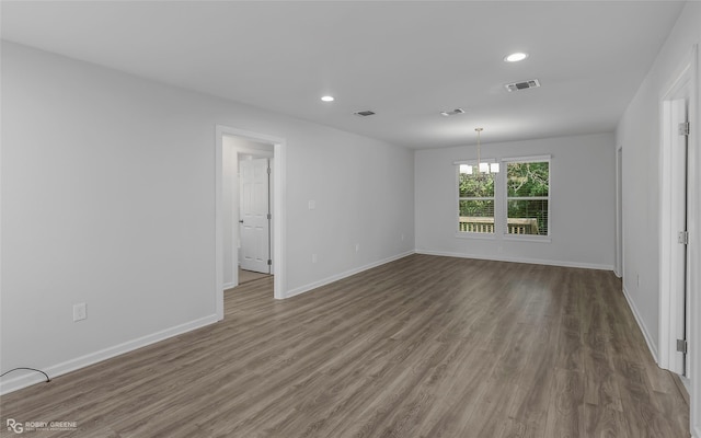 spare room with a chandelier, wood finished floors, baseboards, and visible vents