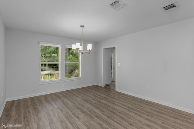 unfurnished room with wood finished floors, a notable chandelier, and visible vents