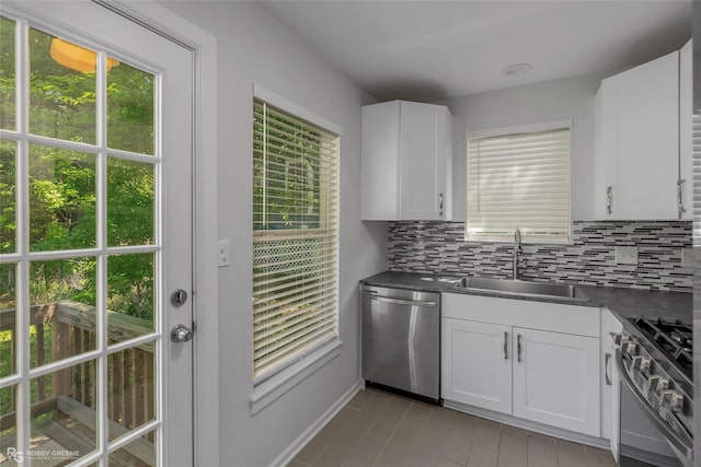kitchen with tasteful backsplash, white cabinetry, dark countertops, stainless steel appliances, and a sink