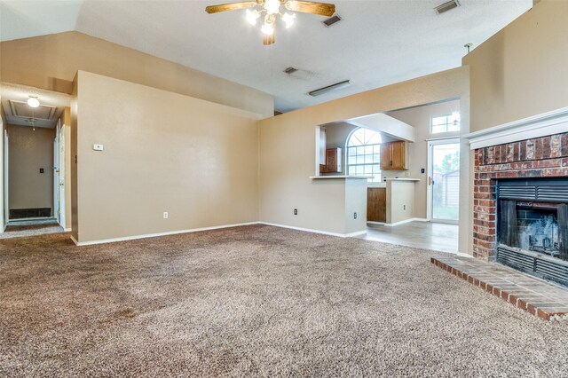 unfurnished living room with light colored carpet, attic access, a fireplace, baseboards, and a ceiling fan