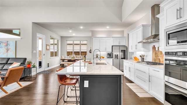 kitchen with a kitchen breakfast bar, wall chimney range hood, white cabinets, a sink, and appliances with stainless steel finishes