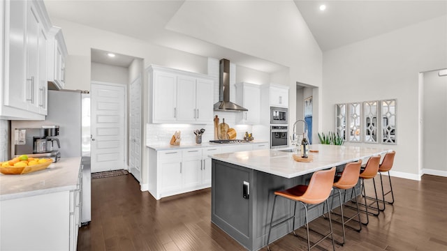 kitchen with wall chimney range hood, appliances with stainless steel finishes, a sink, and white cabinetry
