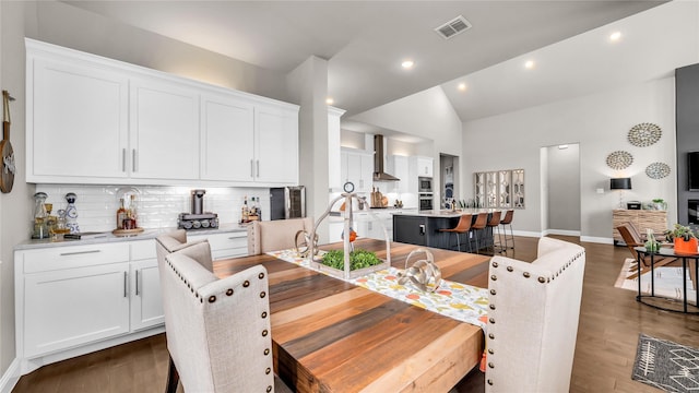 dining space featuring dark wood-style flooring, baseboards, visible vents, and vaulted ceiling