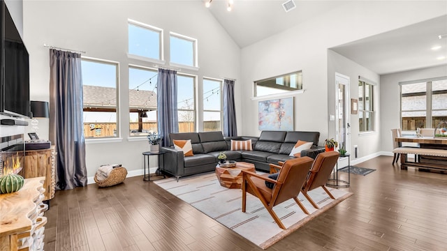 living area with baseboards, visible vents, wood finished floors, and high vaulted ceiling