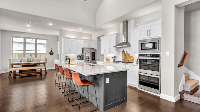 kitchen with wall chimney range hood, dark wood-style flooring, appliances with stainless steel finishes, a breakfast bar area, and white cabinetry