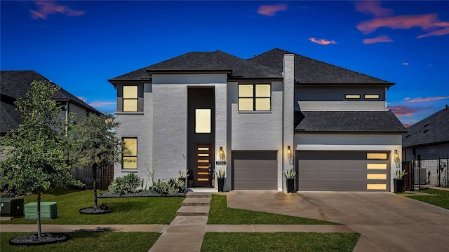 modern home with a garage, fence, roof with shingles, concrete driveway, and a yard
