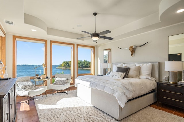 tiled bedroom with a water view, a tray ceiling, multiple windows, and recessed lighting