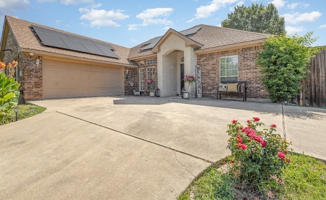 view of front facade with driveway, an attached garage, brick siding, solar panels, and fence