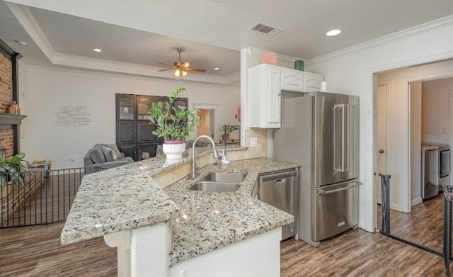 kitchen featuring a sink, a peninsula, white cabinetry, wood finished floors, and stainless steel appliances