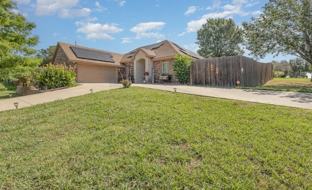 view of front of home with roof mounted solar panels, fence, a front lawn, an attached garage, and concrete driveway