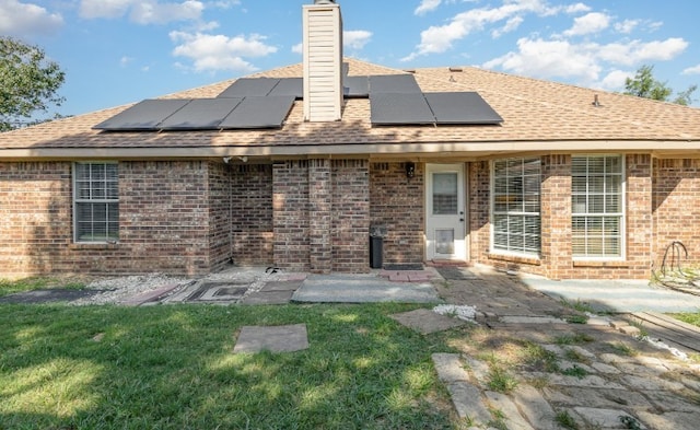 back of property featuring a shingled roof, a yard, a chimney, a patio, and brick siding