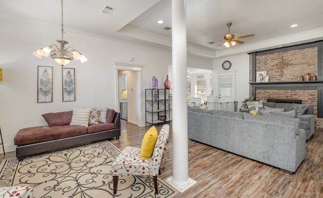 living area with ceiling fan with notable chandelier, wood finished floors, crown molding, and a raised ceiling