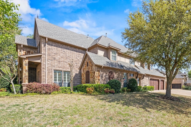 english style home featuring a front lawn, brick siding, roof with shingles, and concrete driveway
