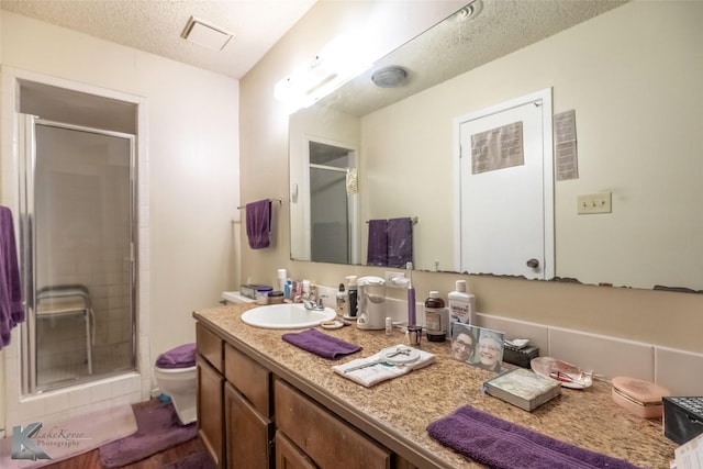 full bath featuring a textured ceiling, toilet, visible vents, a shower stall, and vanity