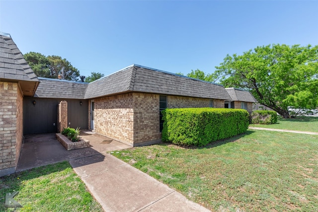 view of side of home featuring a shingled roof, brick siding, a yard, and mansard roof