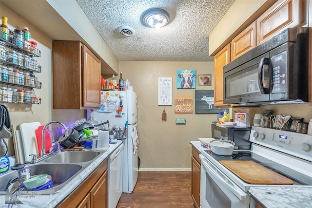 kitchen featuring light countertops, a textured ceiling, a sink, and white appliances