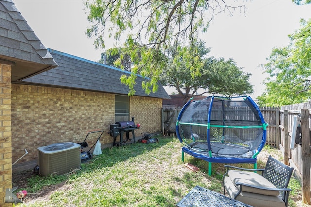 view of yard featuring a fenced backyard, central AC, and a trampoline