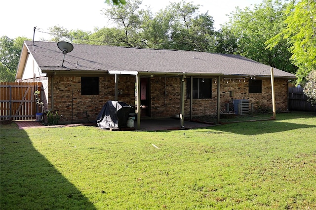 back of house with brick siding, fence, a shingled roof, a patio area, and a lawn
