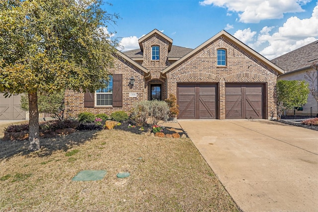 traditional-style home with a shingled roof, driveway, brick siding, a front yard, and a garage