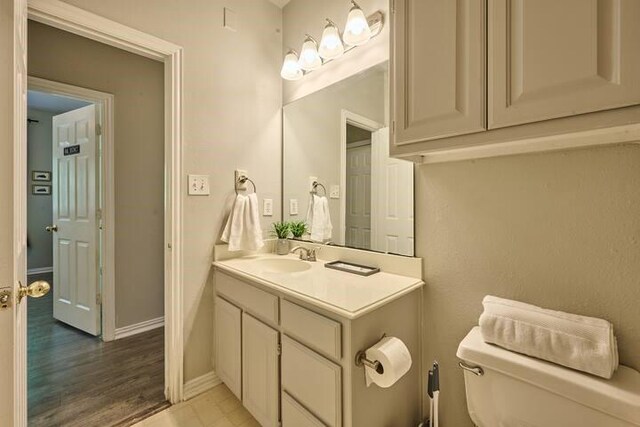 bathroom featuring toilet, baseboards, wood finished floors, and vanity