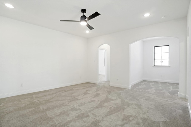 empty room featuring arched walkways, light colored carpet, a ceiling fan, recessed lighting, and baseboards