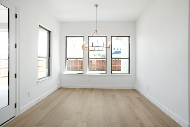 unfurnished dining area featuring light wood-style flooring, baseboards, and an inviting chandelier