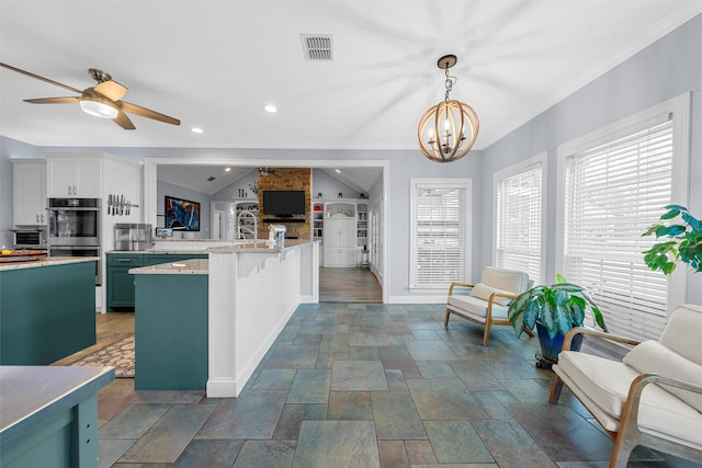 kitchen with stainless steel double oven, visible vents, stone tile flooring, a peninsula, and ceiling fan with notable chandelier