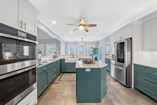 kitchen with a sink, crown molding, green cabinets, appliances with stainless steel finishes, and ceiling fan