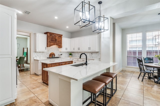 kitchen with visible vents, a notable chandelier, a sink, a center island with sink, and backsplash