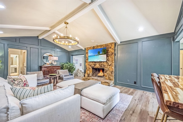 living area featuring lofted ceiling with beams, a decorative wall, light wood-type flooring, a chandelier, and a fireplace