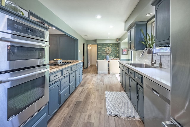 kitchen featuring light countertops, backsplash, light wood-style floors, appliances with stainless steel finishes, and a sink