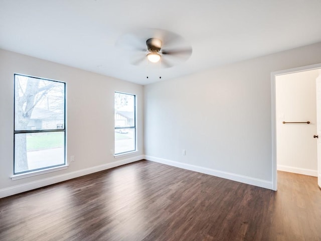 empty room featuring baseboards, a ceiling fan, and dark wood finished floors