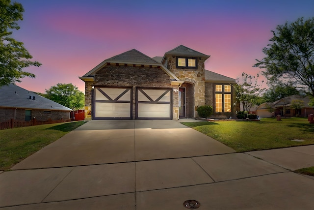 view of front of property featuring stone siding, a garage, a lawn, fence, and driveway