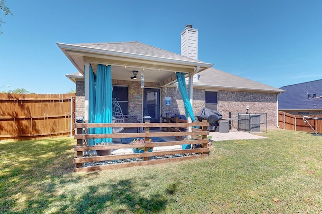 back of property with a fenced backyard, a ceiling fan, a lawn, a patio area, and a chimney