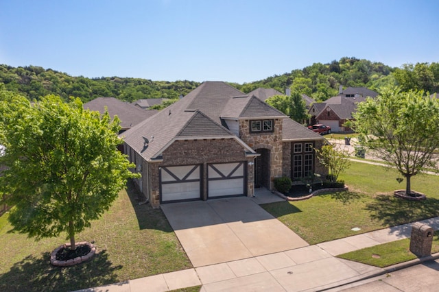 view of front of property featuring stone siding, a front lawn, an attached garage, a shingled roof, and driveway