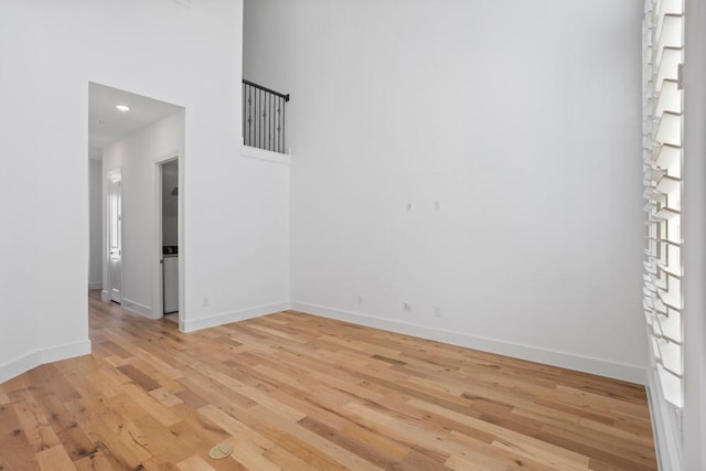 spare room with baseboards, a high ceiling, and light wood-style flooring