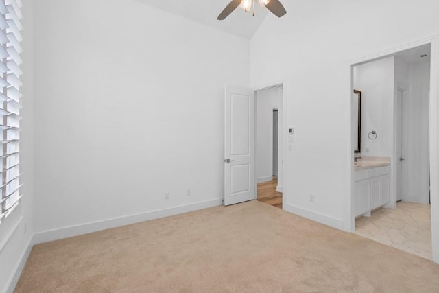 unfurnished bedroom with connected bathroom, light colored carpet, ceiling fan, baseboards, and high vaulted ceiling