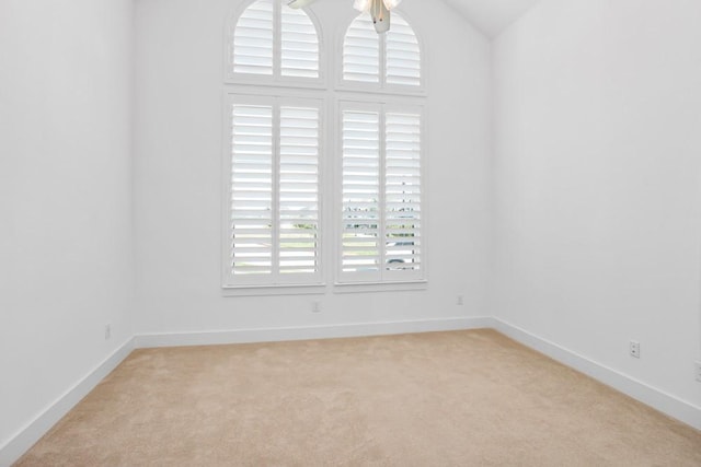empty room featuring baseboards, lofted ceiling, and light colored carpet