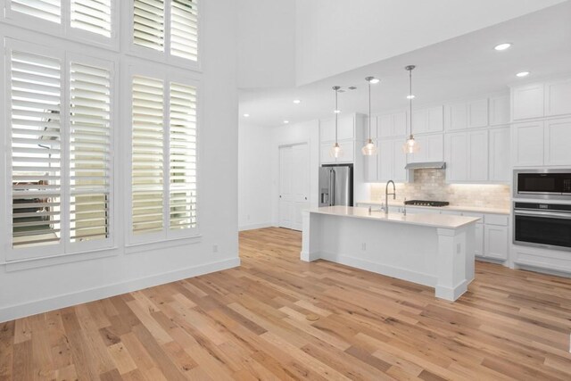 kitchen with tasteful backsplash, decorative light fixtures, light wood-style flooring, light countertops, and appliances with stainless steel finishes