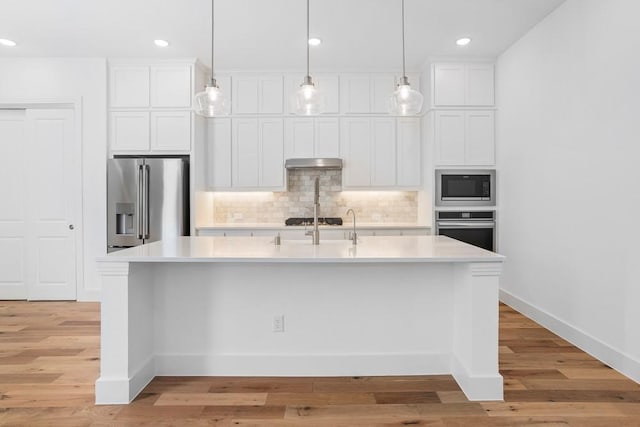 kitchen featuring decorative backsplash, white cabinets, appliances with stainless steel finishes, light countertops, and under cabinet range hood
