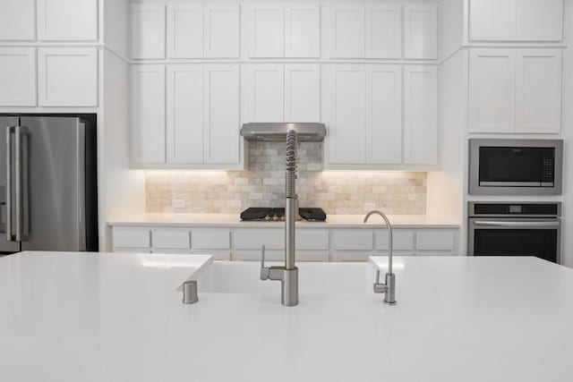 kitchen with decorative backsplash, white cabinetry, stainless steel appliances, and light countertops