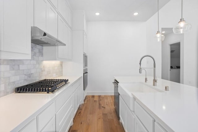 kitchen featuring appliances with stainless steel finishes, a sink, light countertops, and under cabinet range hood