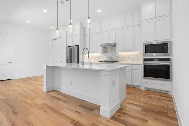 kitchen featuring decorative backsplash, under cabinet range hood, appliances with stainless steel finishes, light countertops, and light wood-type flooring