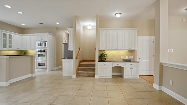 kitchen with decorative backsplash, dark countertops, built in study area, stainless steel appliances, and white cabinetry