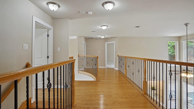 hall featuring visible vents, light wood-style flooring, baseboards, and an upstairs landing