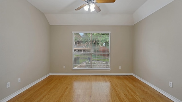 spare room featuring baseboards, a ceiling fan, light wood-style flooring, and vaulted ceiling