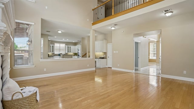 unfurnished living room with a high ceiling, a fireplace, light wood-style flooring, baseboards, and visible vents