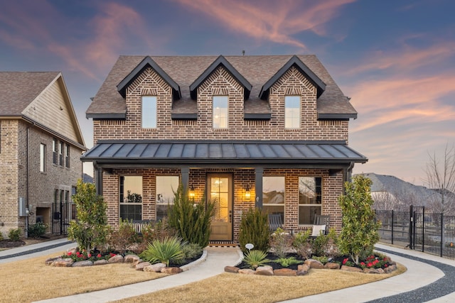 view of front of home with a standing seam roof, brick siding, and fence